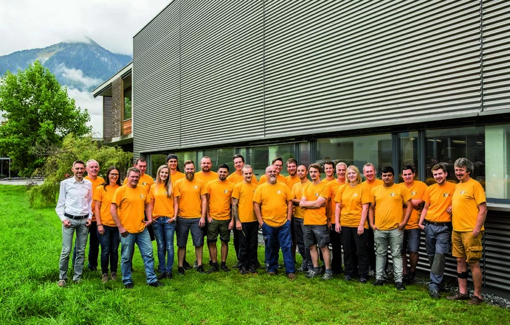 Gruppenfoto des Teams von FETZEL Maschinenbau. Ca. 30 Mitarbeiter in orangen T-Shirts vor dem Firmengebäude.